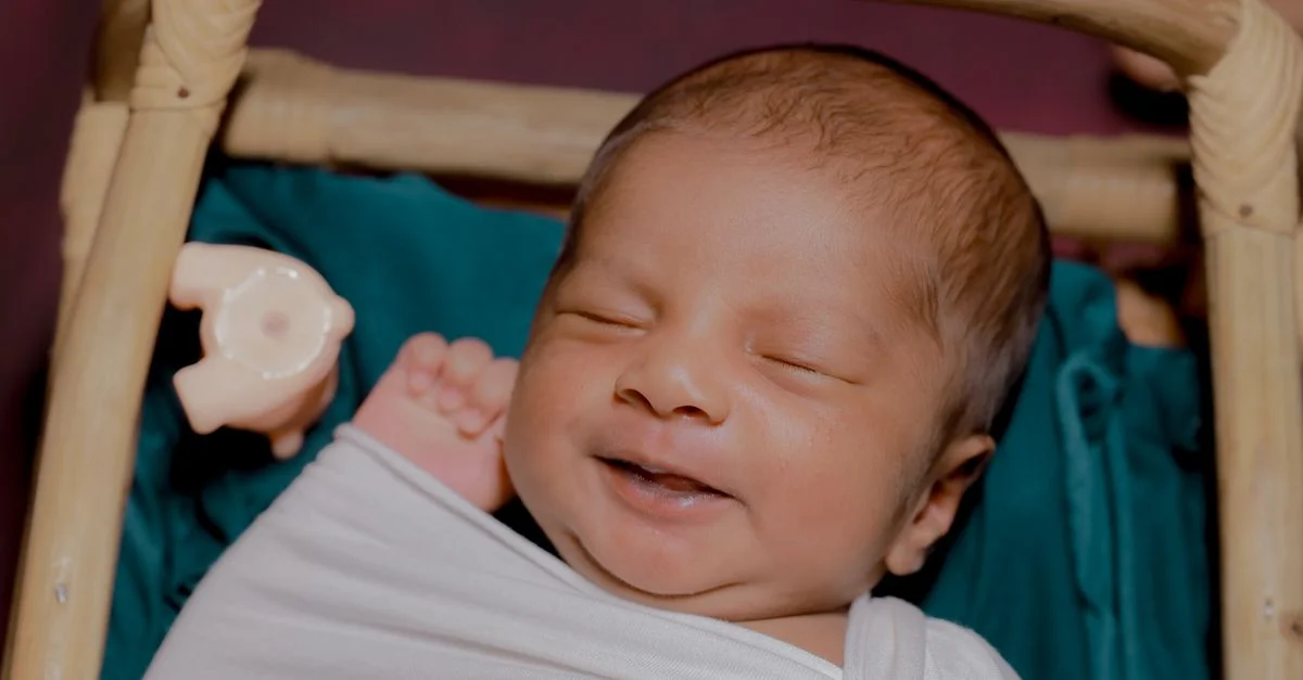 Un bebé sudasiático alegre sonriendo pacíficamente en una cuna interior, envuelto en una manta.