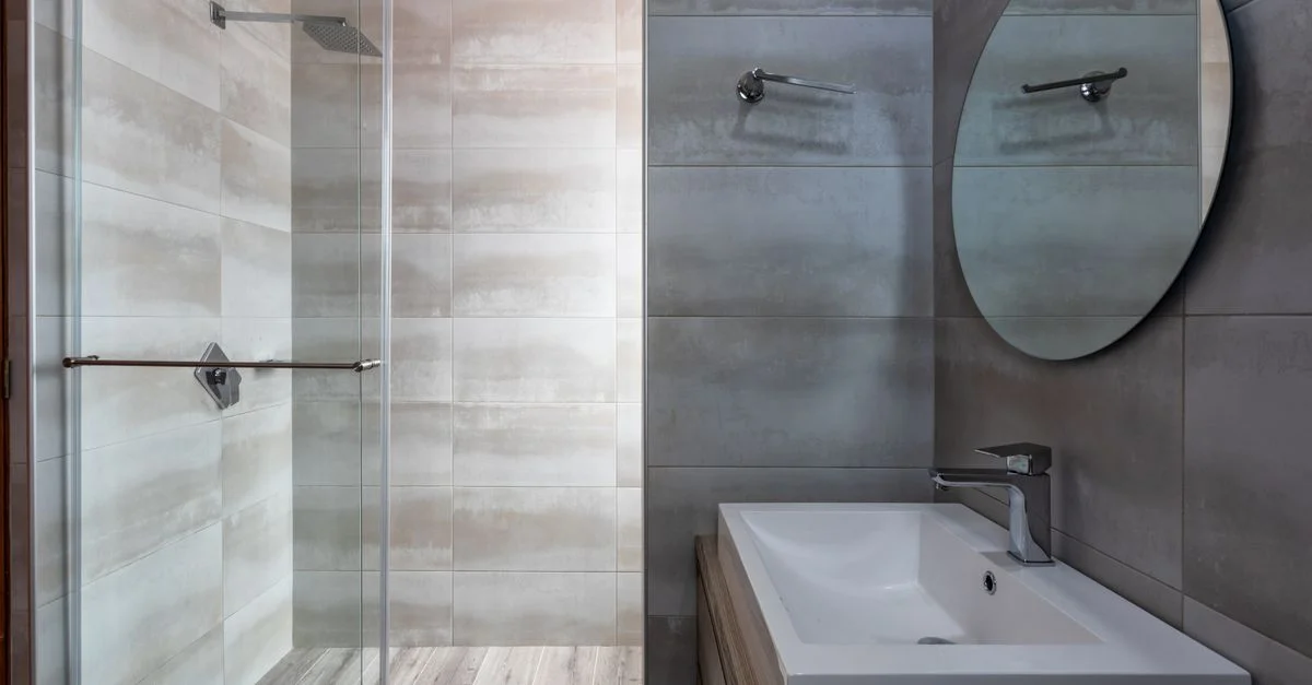 Baño moderno elegante con ducha de cristal, espejo redondo y lavabo elegante.