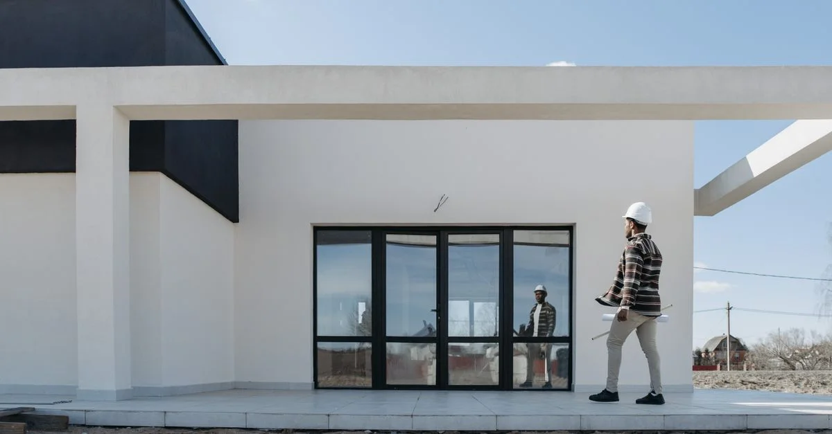 Arquitecto con casco evaluando la fachada de una casa moderna. Ideal para temas de construcción y arquitectura.