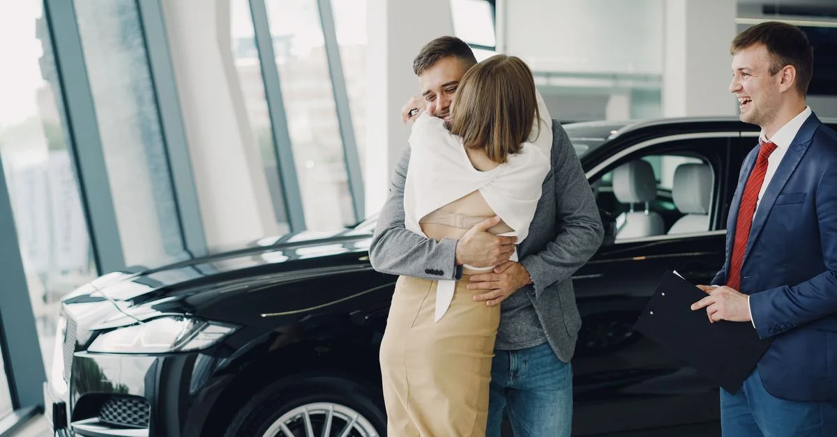 Una pareja se abraza con alegría en un concesionario de coches tras comprar un vehículo nuevo.