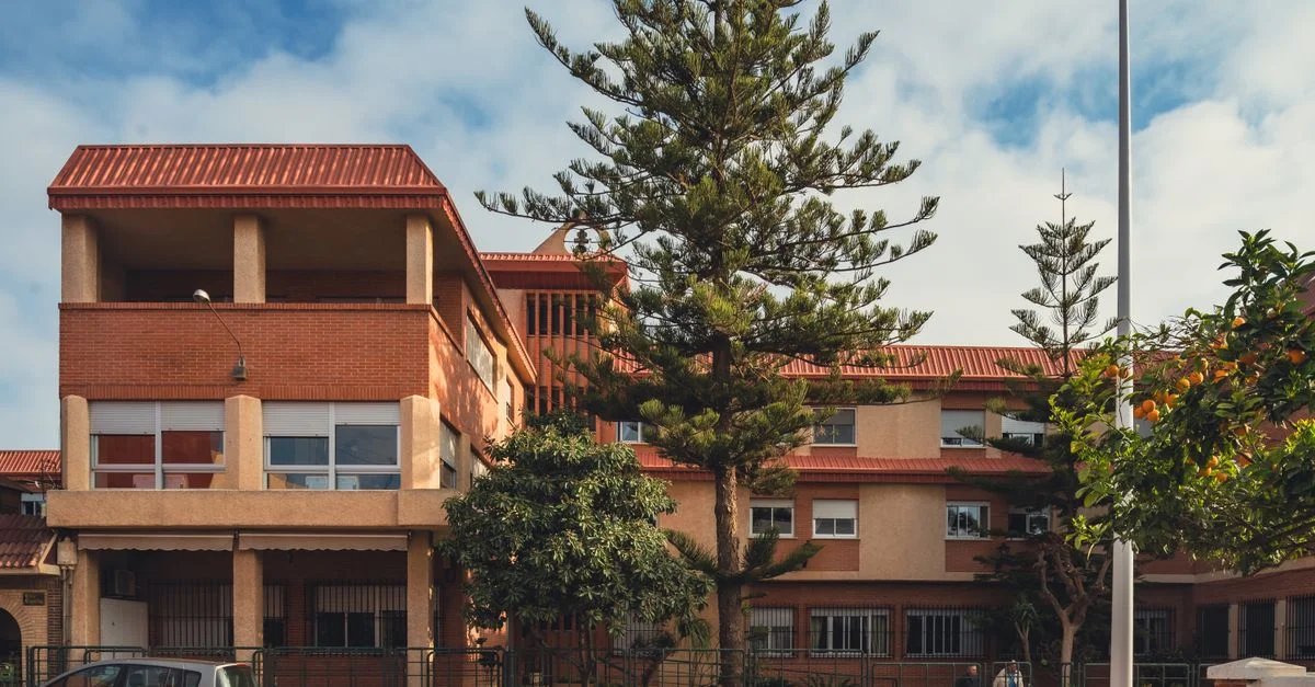 Una vista soleada de una calle con un edificio residencial de techo naranja y árboles en San Javier, España.