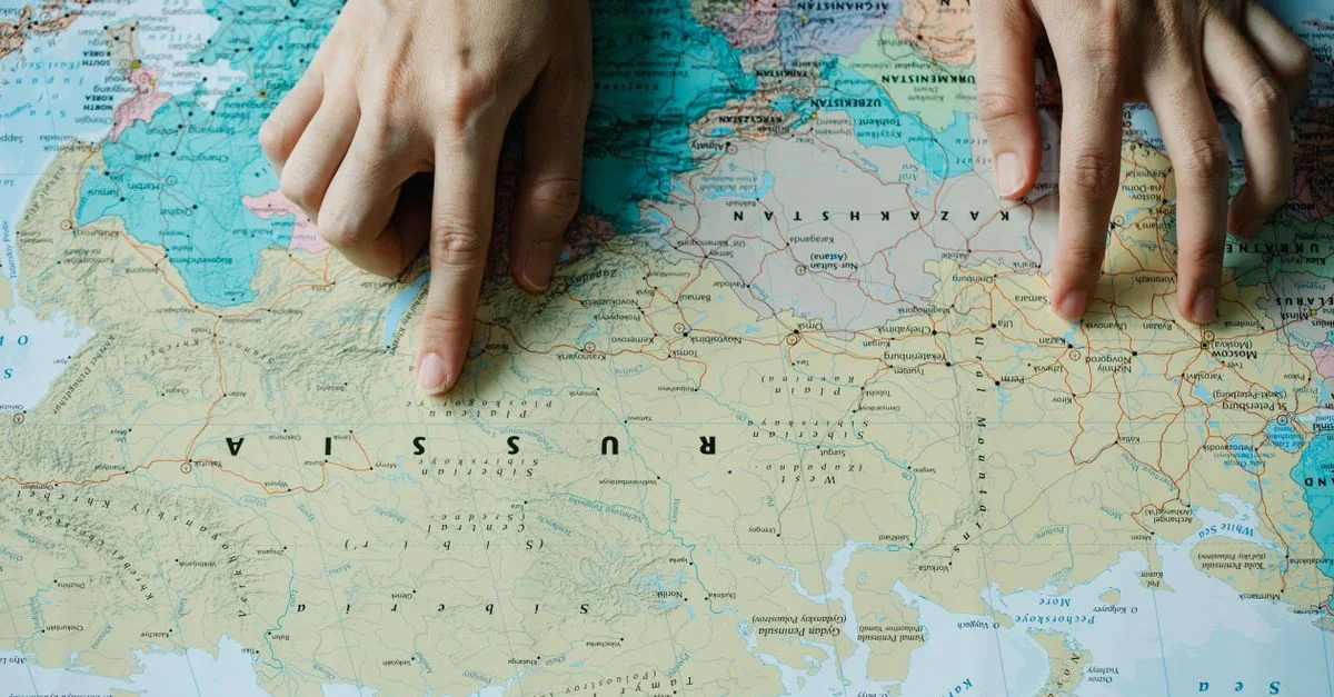 Primer plano de manos apuntando a Rusia en un mapa mundial detallado.