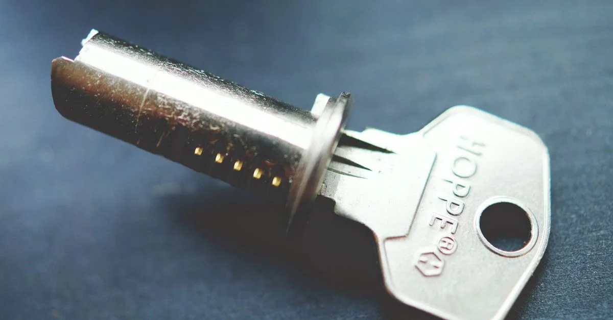 Imagen detallada en primer plano de una llave metálica con cilindro de cerradura sobre una superficie oscura, resaltando detalles intrincados.