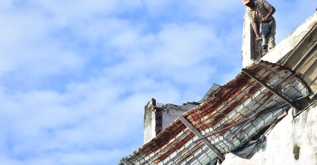 Un hombre está de pie en un tejado bajo un cielo azul claro, mostrando contraste y textura.