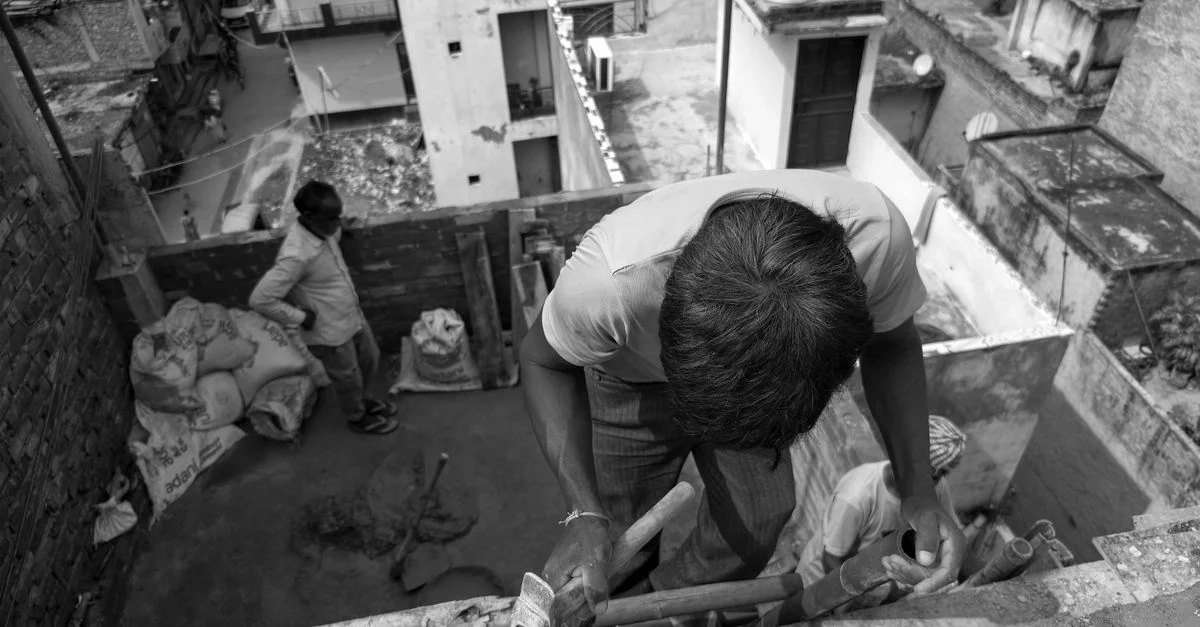 Un obrero de la construcción colocando ladrillos en una azotea urbana, en blanco y negro.