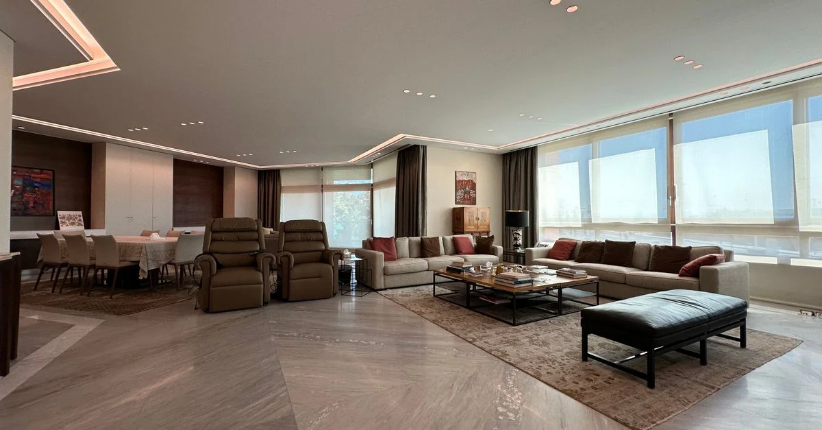 Elegante y espaciosa sala de estar moderna con ventanas panorámicas, muebles elegantes e iluminación cálida, creando un ambiente acogedor.