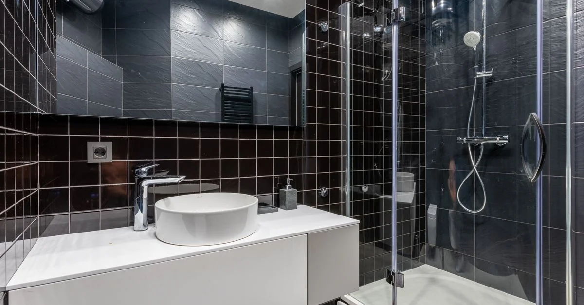 Baño elegante con azulejos negros, ducha de vidrio y accesorios modernos.