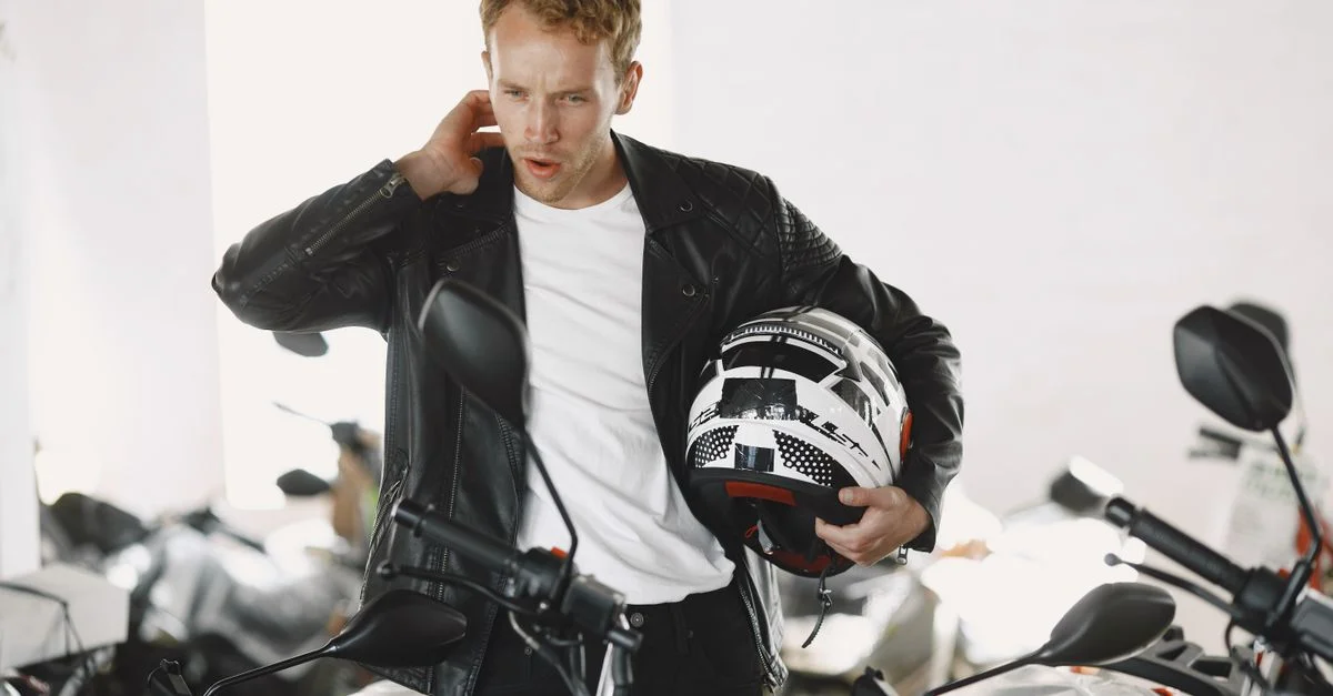 Un hombre con una chaqueta de cuero examina una motocicleta en una sala de exposición de concesionarios.